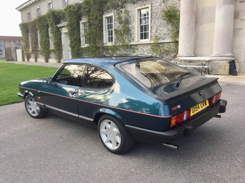 Rear view of green Ford Capri parked in front of stone building