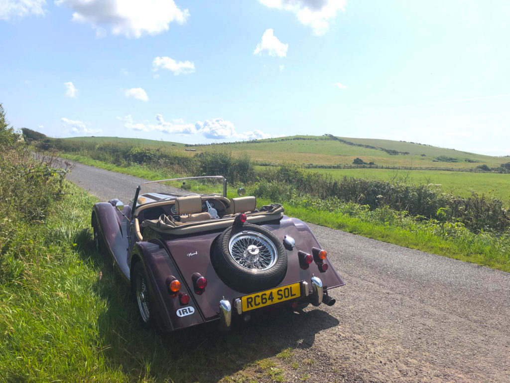 Morgan car parked on grass verge overlooking hills and fields