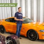 Main stood next to parked up orange car in a garage