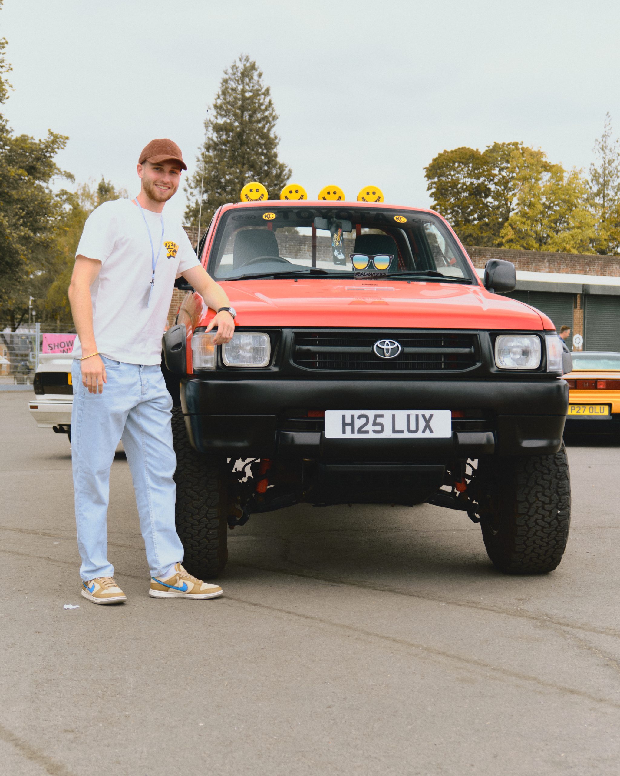 Man leaning against a parked red pickup truck with trees in the background