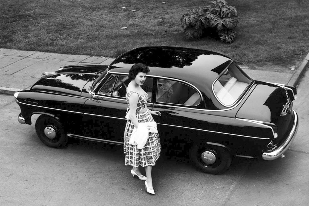 Woman standing in front of parked car on a road next to grass verge