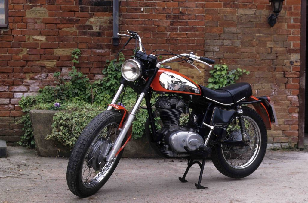 Red classic motorbike parked in courtyard in front of red brick building
