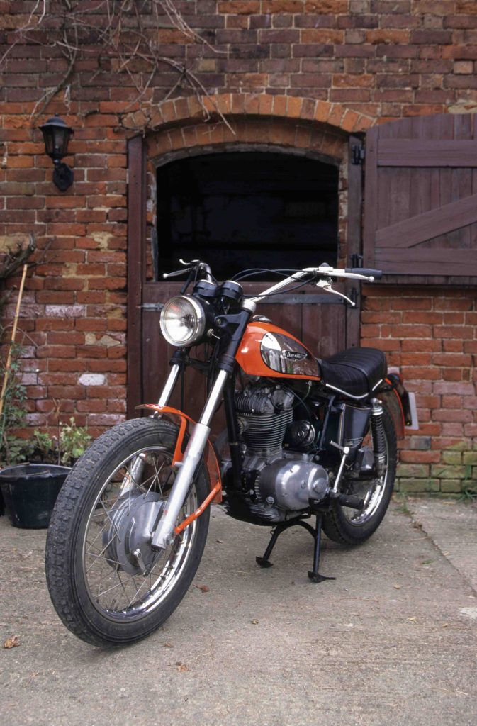 Red classic motorbike parked in courtyard in front of red brick building