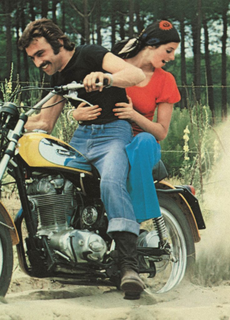 Rider and pillion riding yellow classic motorbike on dirt track