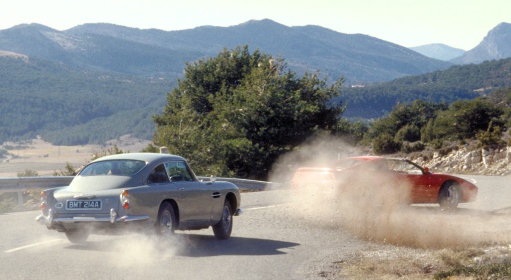 Two cars driving through mountain roads with dust clouds