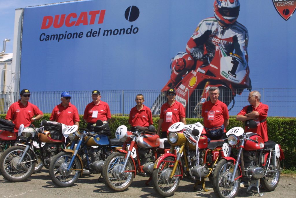 Five motorbikes parked with seven men standing outside museum