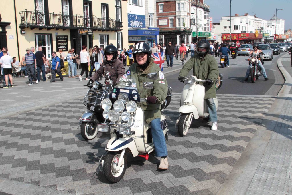 Three riders on scooters driving along busy road