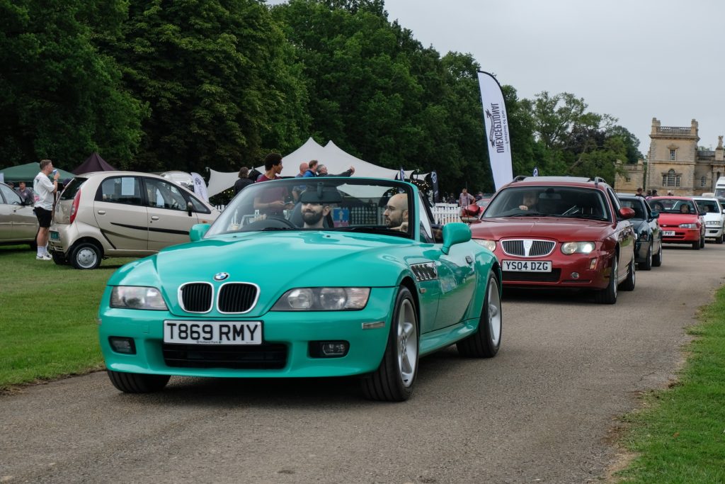 Five cars lined up on a long tarmac driveway next to grass verge