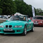 Five cars lined up on a long tarmac driveway next to grass verge