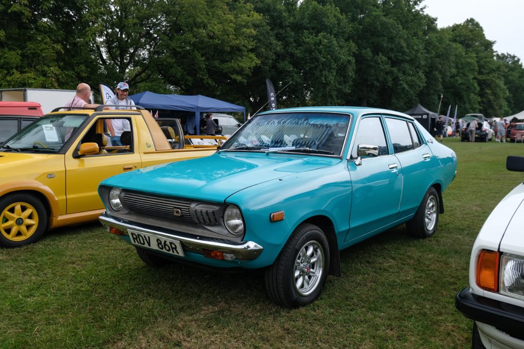 A blue and a yellow car parked in a field with trees in the background