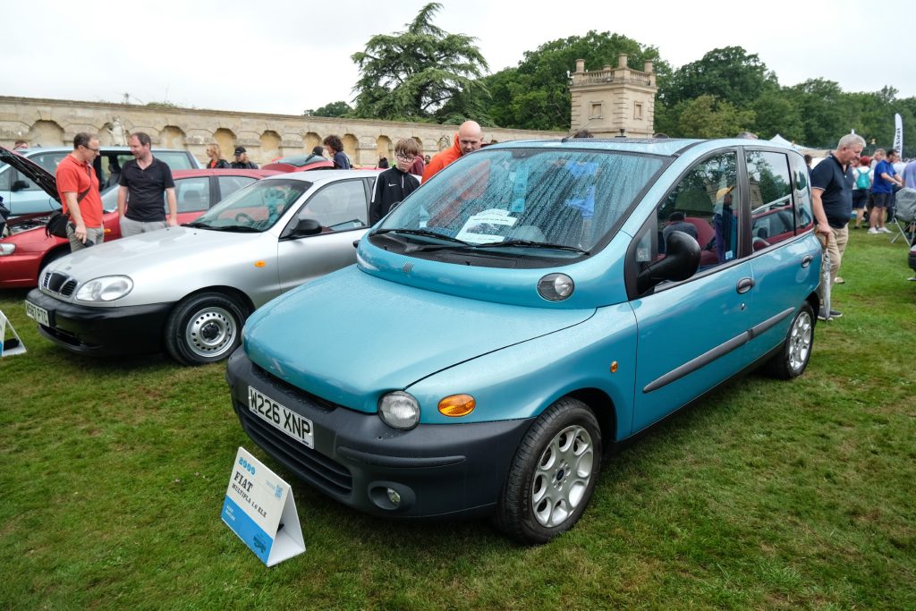 Group of people standing next to several cars parked in a row