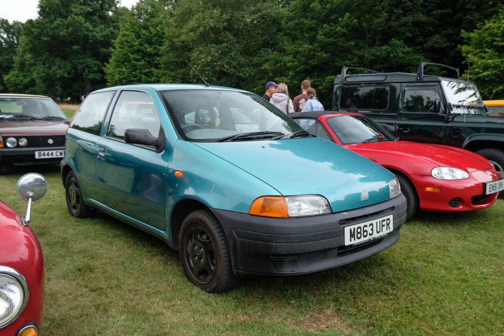 Group of people standing next to three cars parked in a row