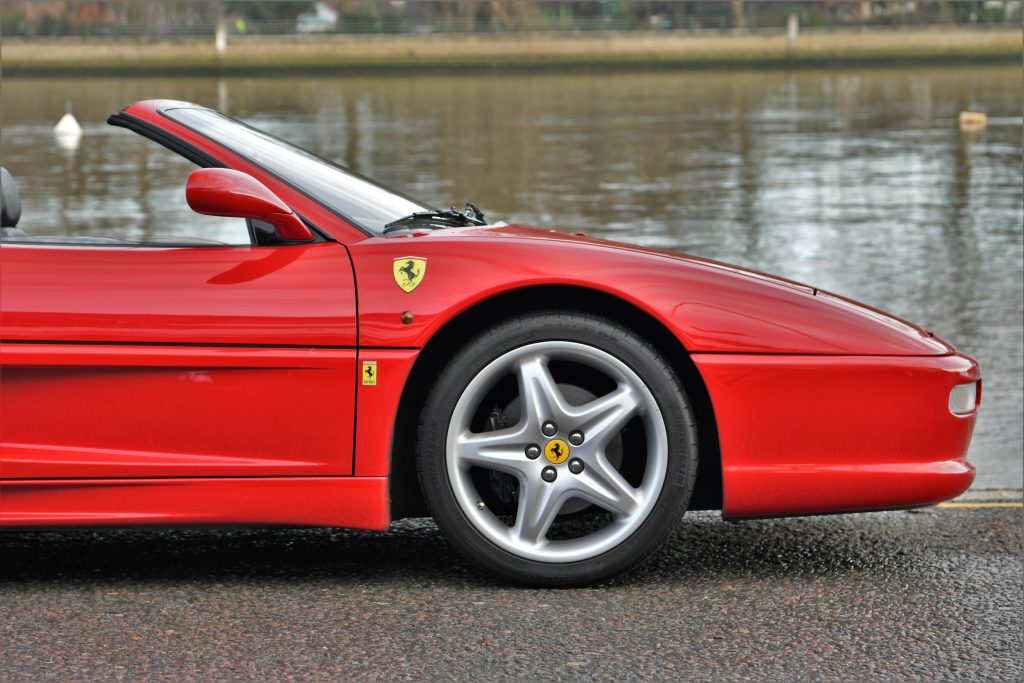 Side view of red Ferrari F355 Spider parked in front of a lake 