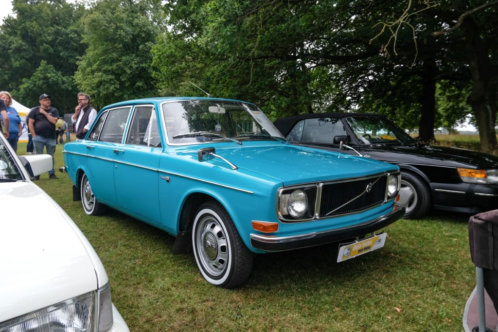 Three cars parked in a row in grass field with trees behind