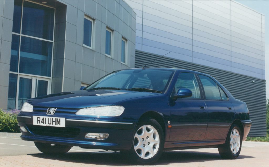 Blue Peugeot 406 V6 parked in front of a modern grey building
