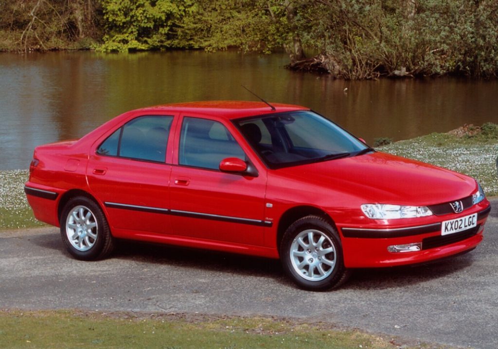 Red Peugeot 406 parked on tarmac road in front of a lake