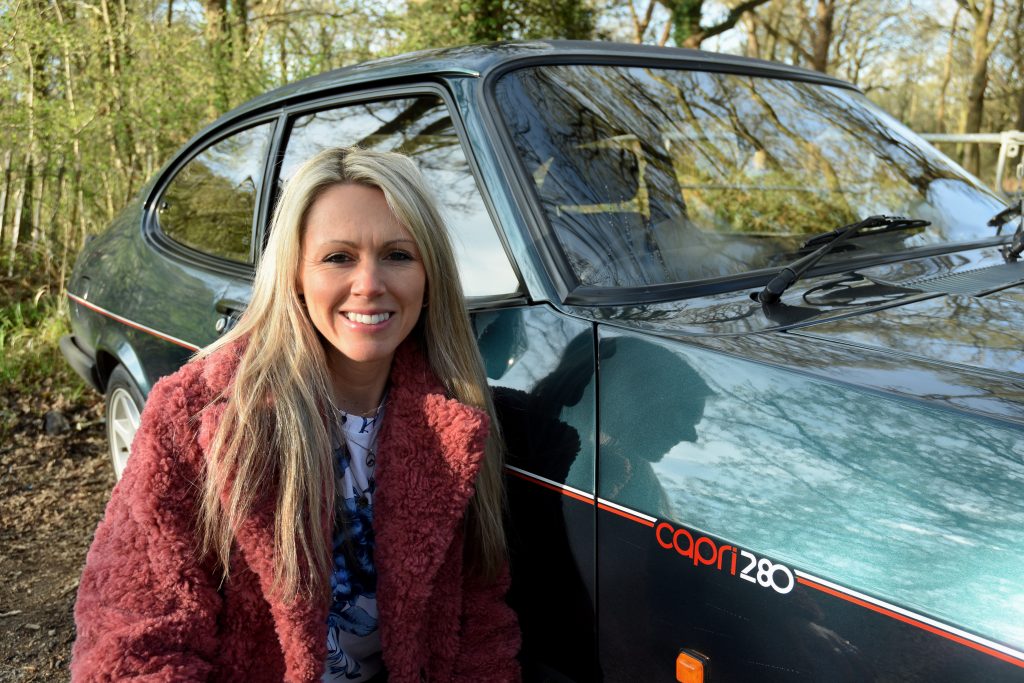 Woman smiling kneeling next to a green car