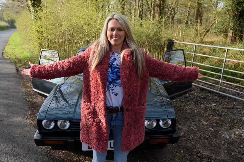 Woman stood next to a green car in woodland