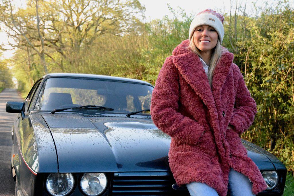 Woman perched on the front of a green car in woodland