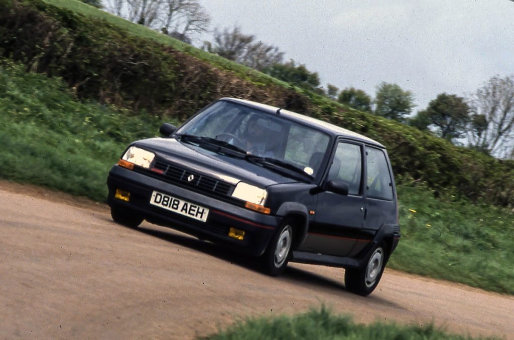Black car driving along dirt track with grass verge and hedges behind