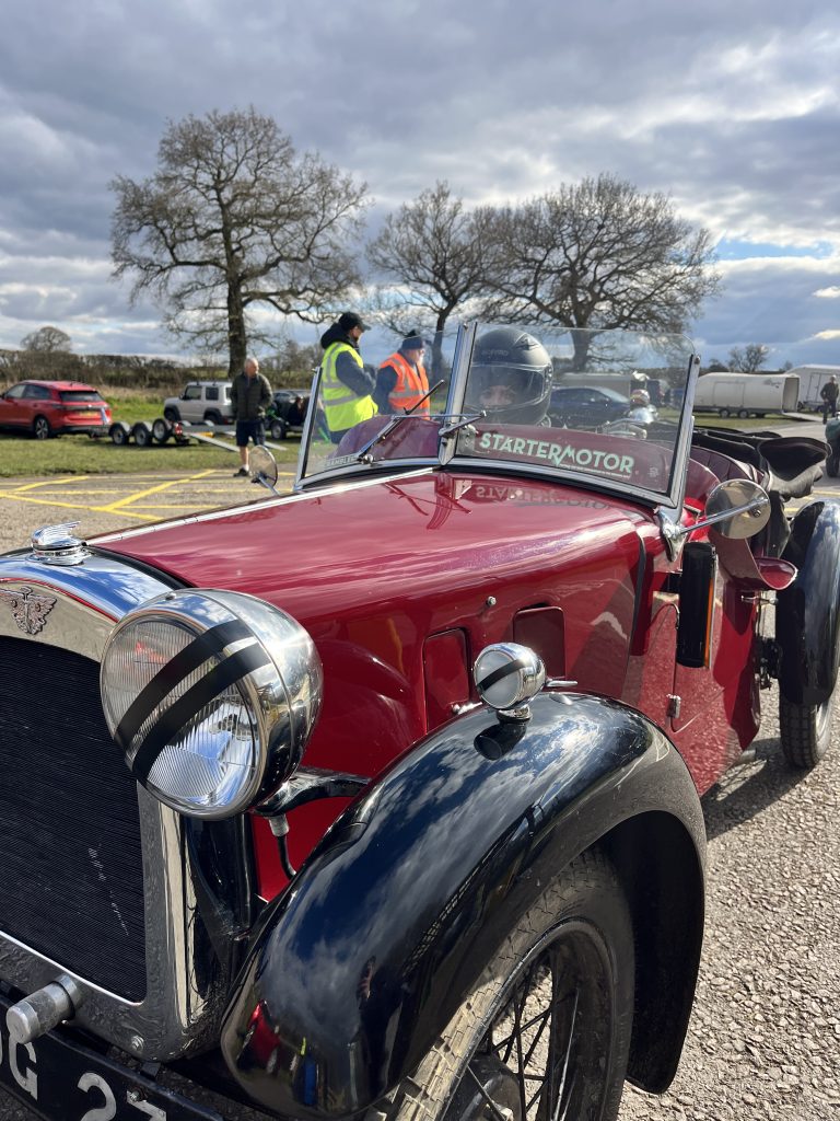Front view of a red classic car with open top and a driver inside