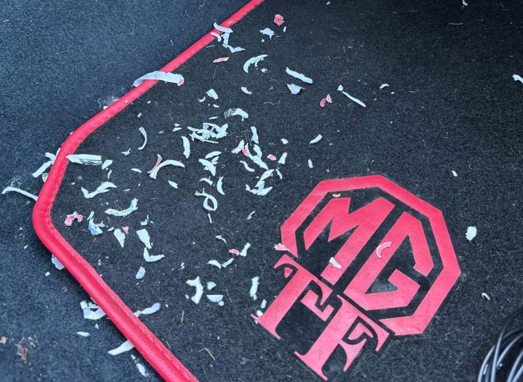 Chewed up plastic on the carpet in a classic car as a result of rodent damage