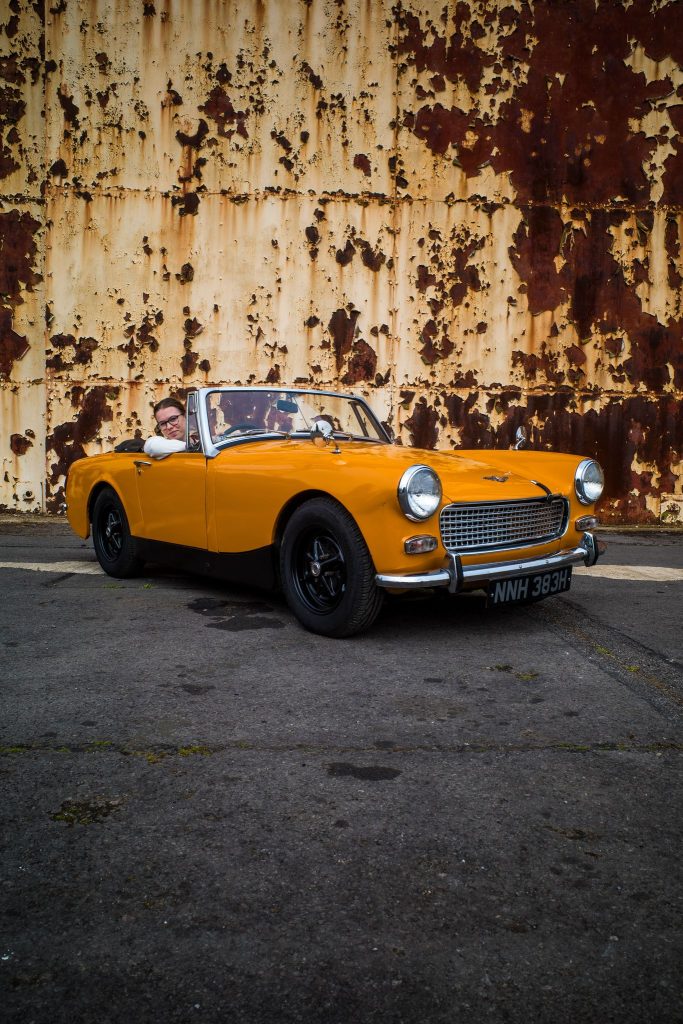 Yellow classic car parked in front of a warehouse