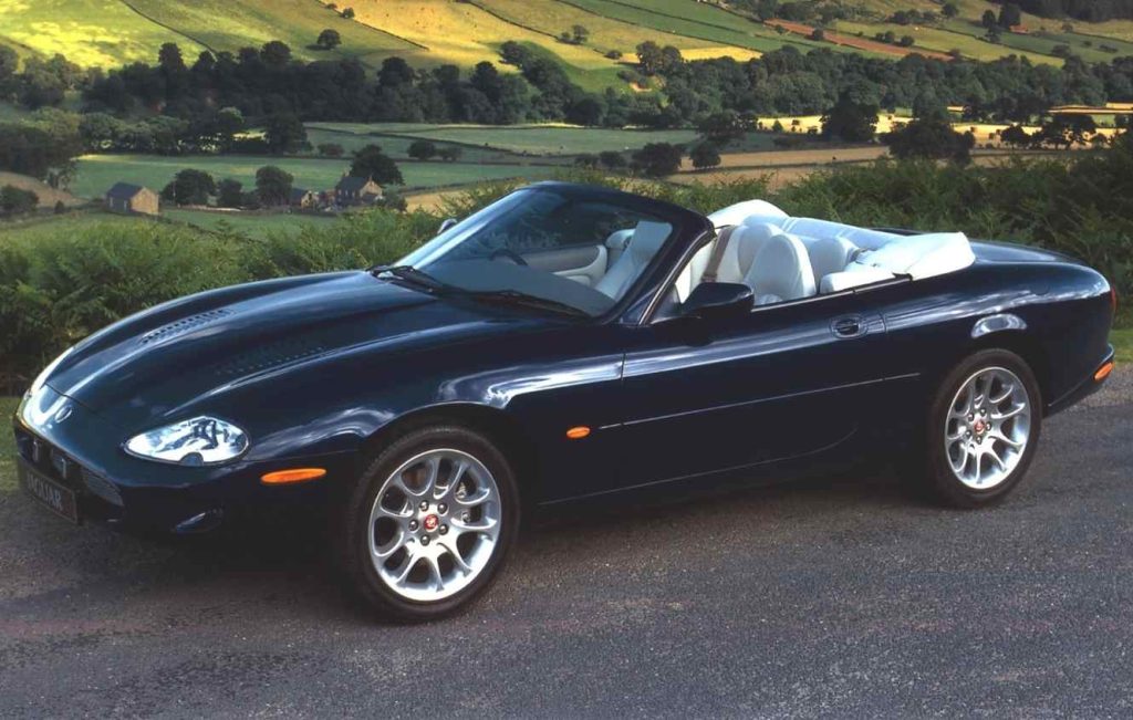 Blue Jaguar XKR convertible parked on a road with fields and trees