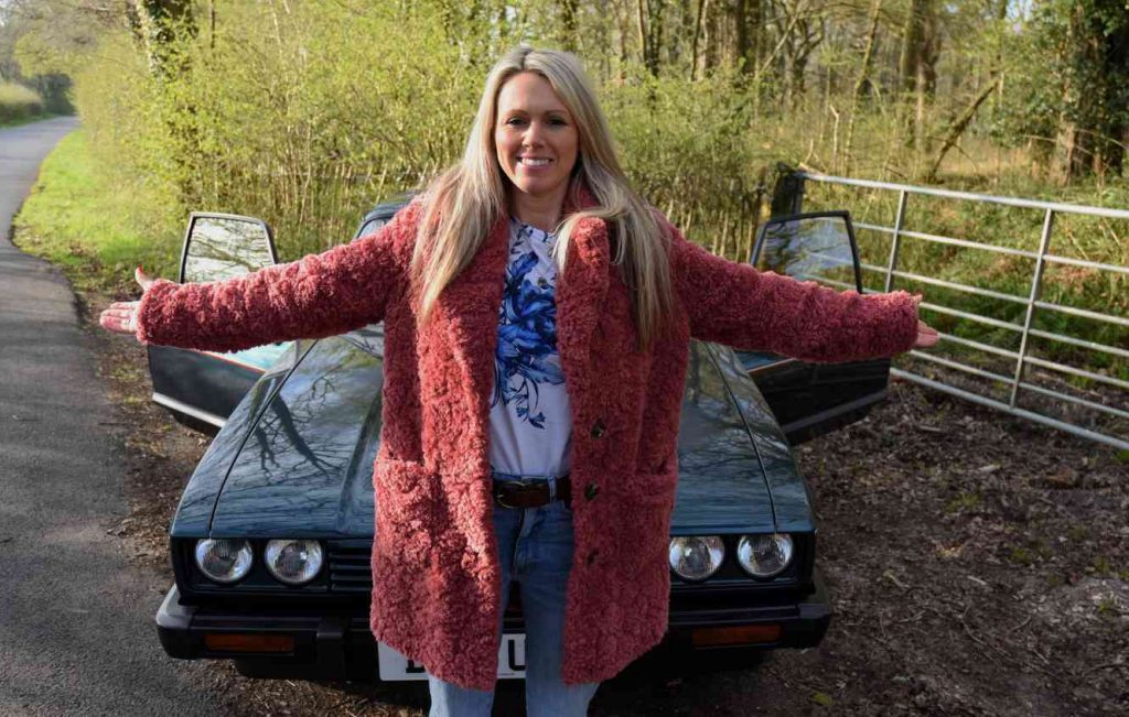 Woman stood next to a green car in woodland