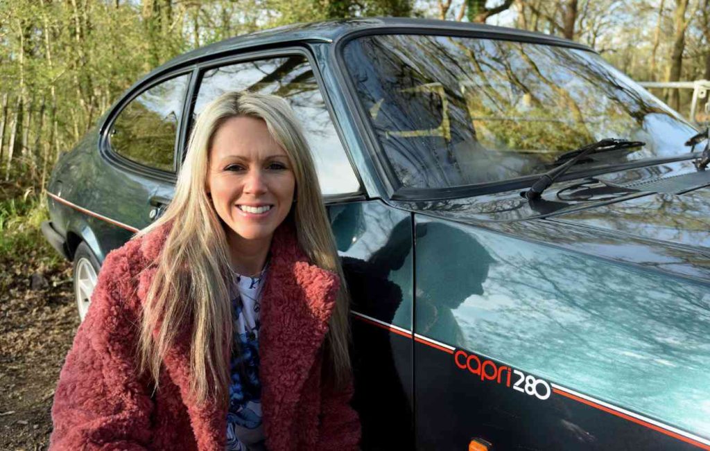 Woman smiling kneeling next to a green car