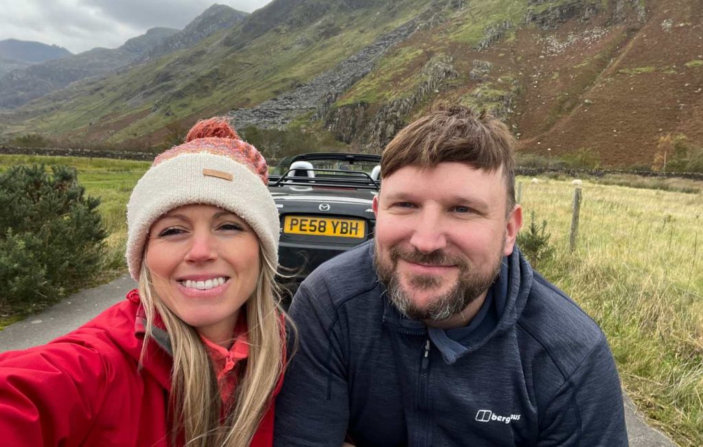 Man and woman smiling in front of parked car