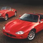Two red Jaguar cars parked on on gravel ground