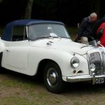 White classic Daimler car parked in a field with two people standing beside it