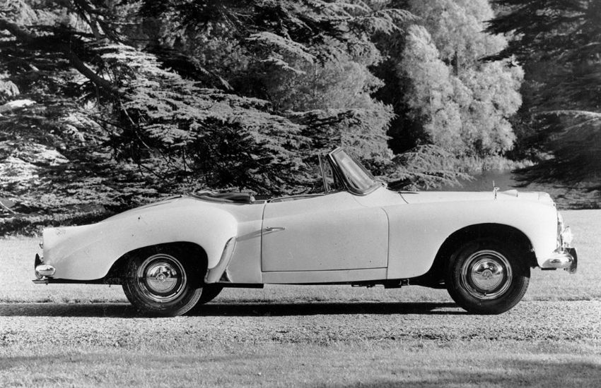 Side view of a convertible classic car parked with trees in the background