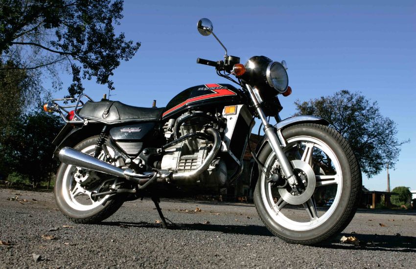 Red and black Honda CX500 motorbike parked up with blue skies and trees in the background