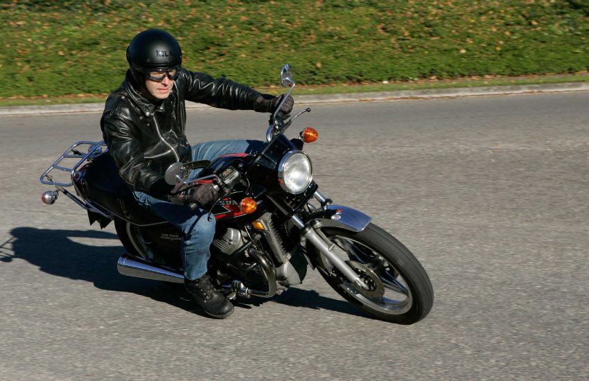Rider riding red and black motorbike around a corner with grass verge in the background