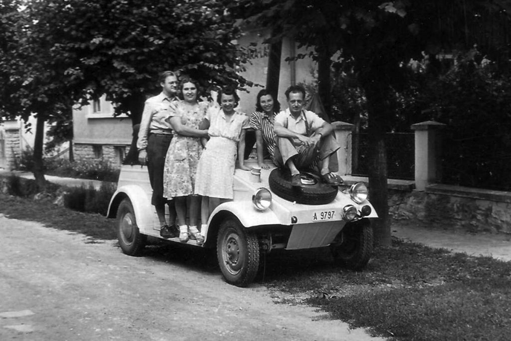 Two men and three women sitting on a parked up classic car