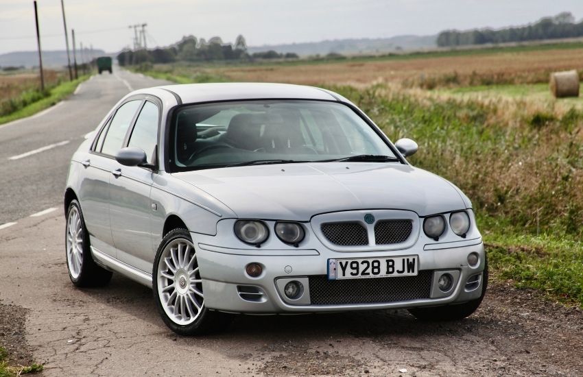 Silver MG Z car parked on the side of a road next to fields