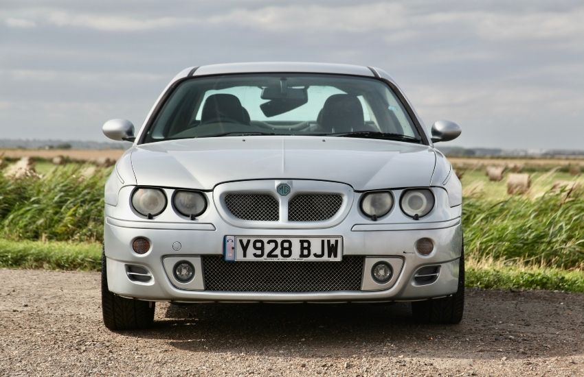 Silver MG Z car parked on gravel road next to fields