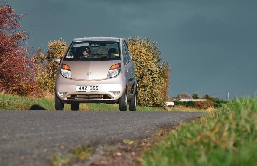 Tata Nano driving along a country lane with bushes in the background
