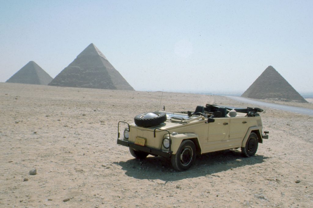 Yellow military Volkswagen vehicle parked in a desert with pyramids in the background