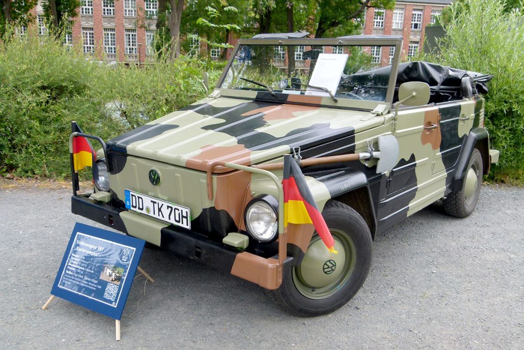 Camouflage military vehicle parked with bushes in the background