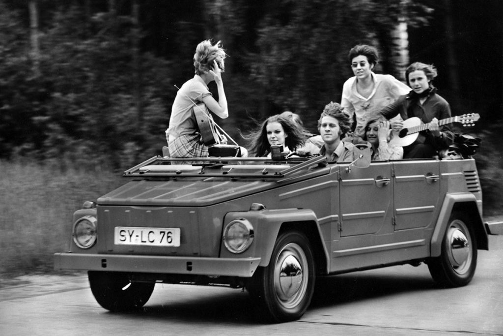 Seven people sitting in an open top car driving along a road