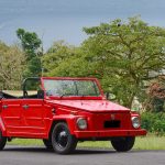 Red Volkswagen Type 181 parked on a road with trees in the background
