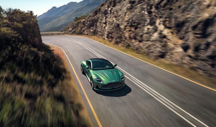 Green Aston Martin DB12 driving along a road going through mountains