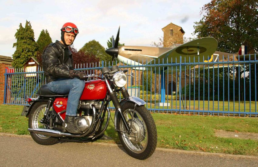 Man sat on top of BSA Spitfire MkIV motorbike in front of a Spitfire plane
