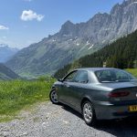 Rear view of an Alfa Romeo car parked on the side over the road overlooking mountains