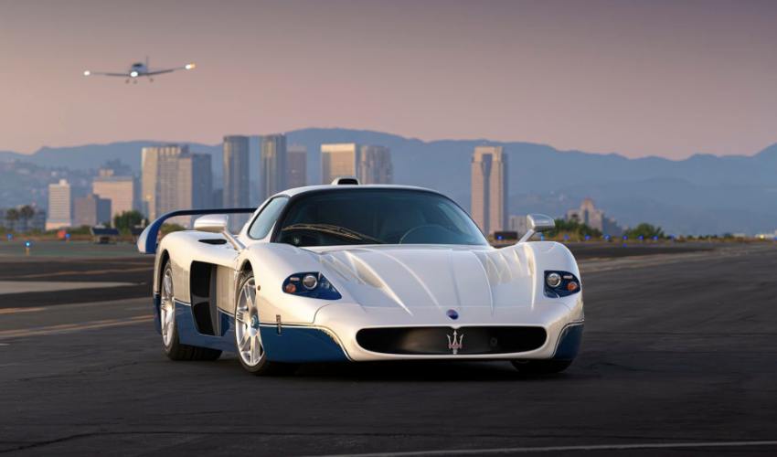 White Maserati MC12 parked on a runway with buildings and mountains in the background