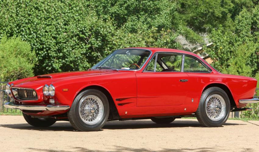 Side view of a red Maserati Sebring parked in front of bushes