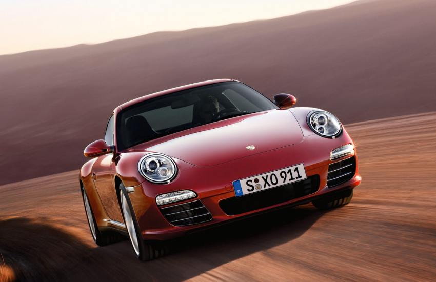 Red Porsche Carrera S driving at speed along a road with mountains in the background